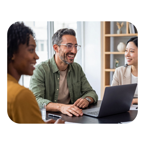 Three professionals smiling during a meeting with a laptop, illustrating tools built to meet the highest hiring compliance standards.